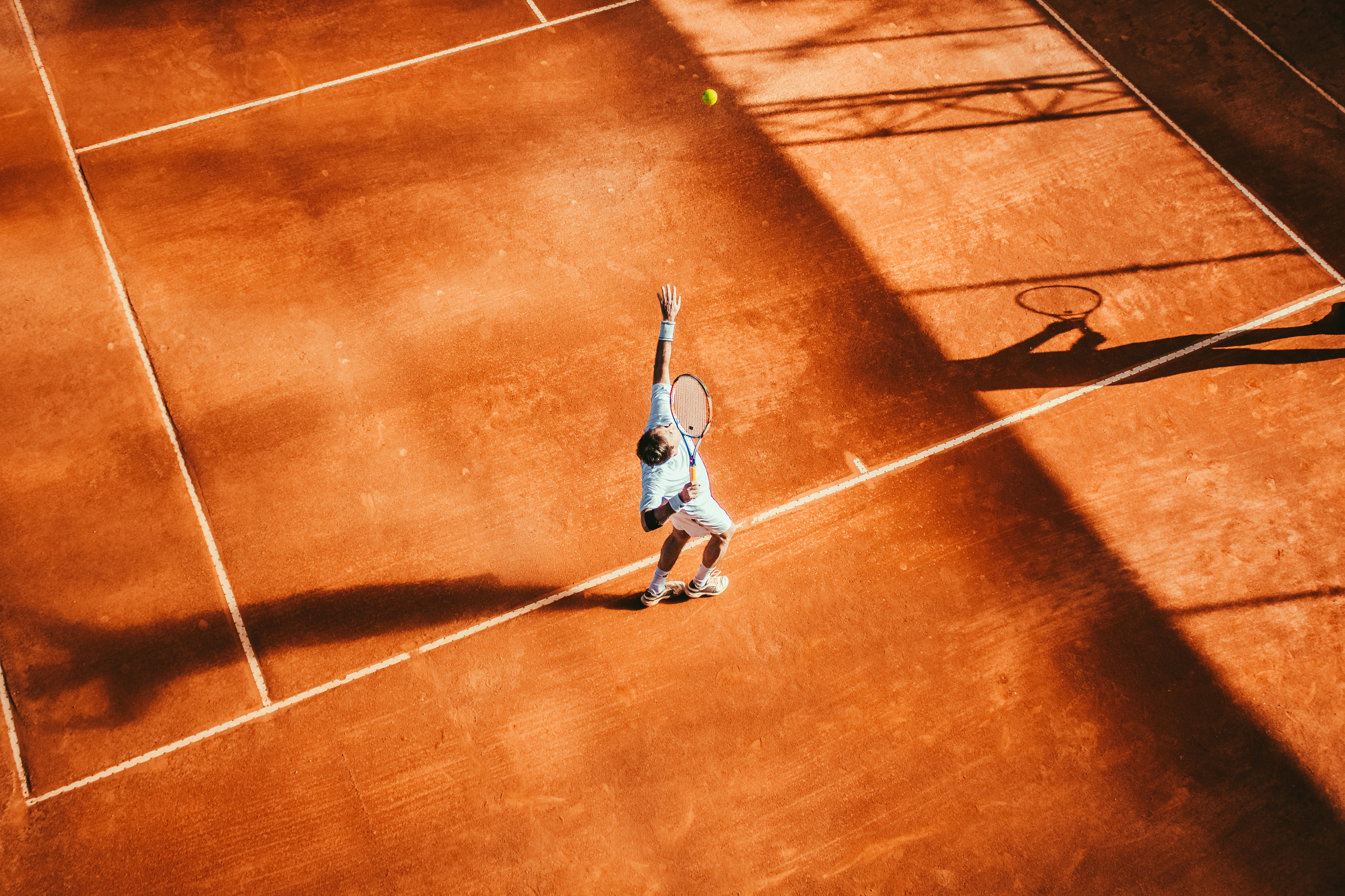 Tennisser serveert op een gravelbaan in het gouden licht aan de Costa del Sol
